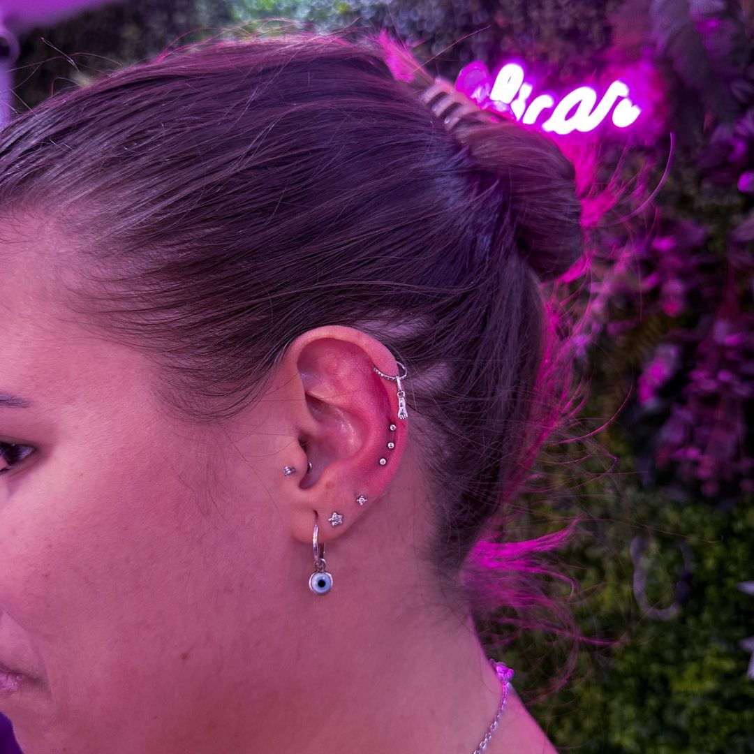 Composição auricular com piercing helix e brinco de olho grego pendente — Luquini Clinic, Rio de Janeiro